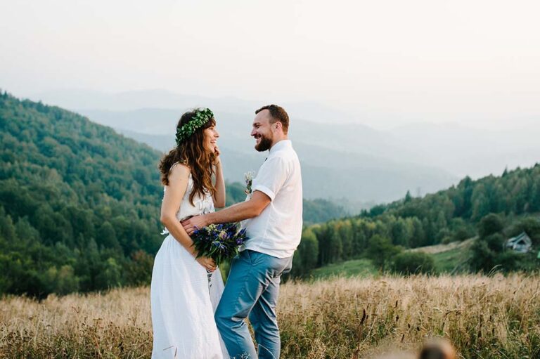 a bride and groom laughing in a field in the mountains