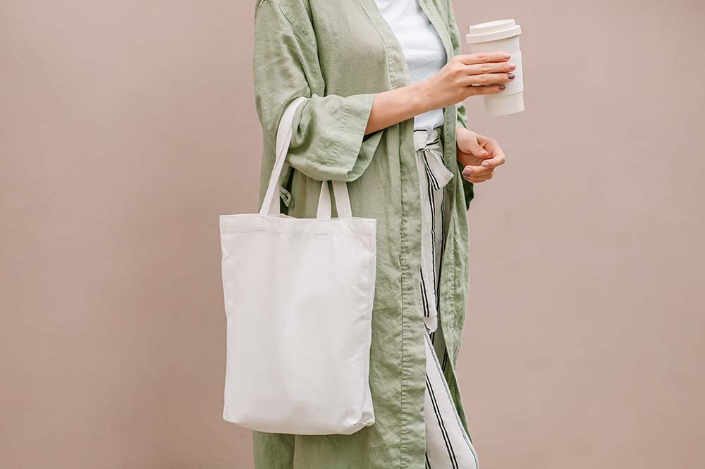 a woman carrying a reusable coffee mug and tote bag