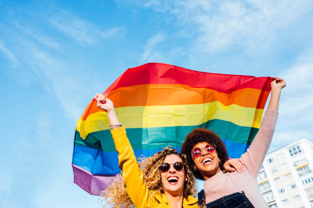two women holding up a rainbow pride flag at a parade