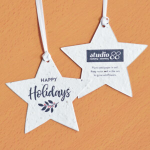 An add-your-logo seed paper ornament in the shape of star with black Happy Holidays text and a festive twig