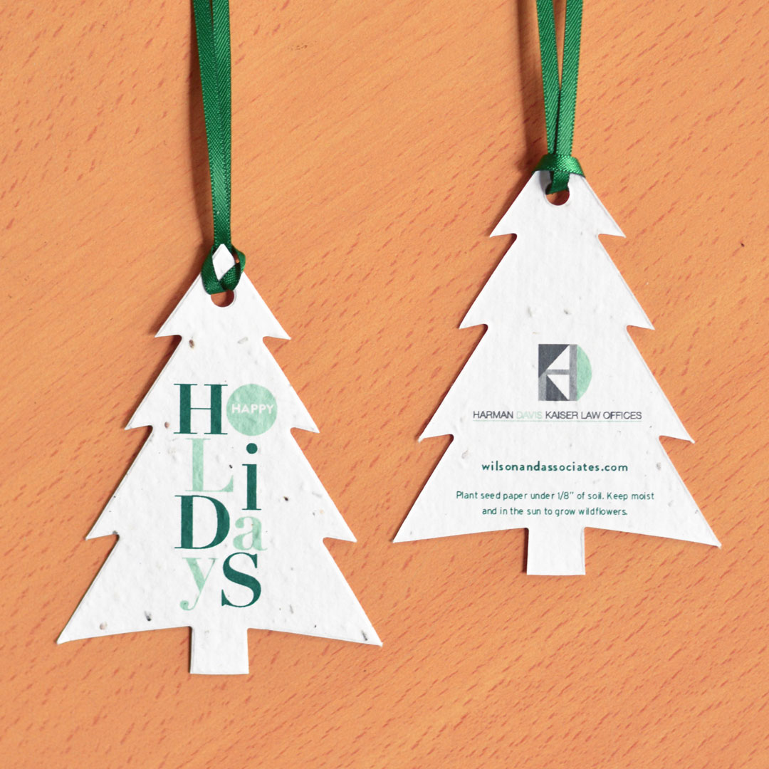 An add-your-logo seed paper ornament in the shape of spruce tree with Happy Holidays lettering in green