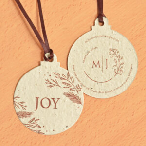 A promotional ornament ball featuring the word JOY with rustic brown botanical accents printed on unbeached twice-recycled seed paper