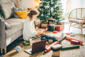 Woman wrapping eco-friendly gifts by a Christmas tree and making notes