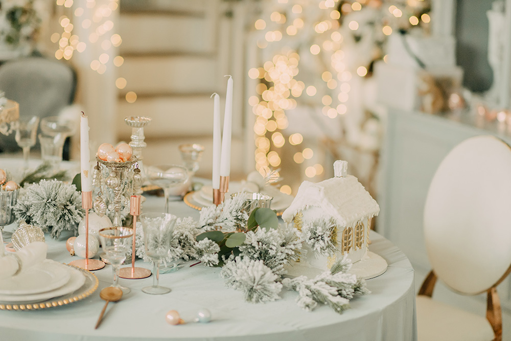 A winter table setting with foliage and candles as a centre piece. Twinkle lights out of focus in the background  