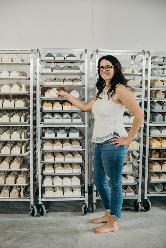 Candance Alarie standing in front of racks of handmade soap.