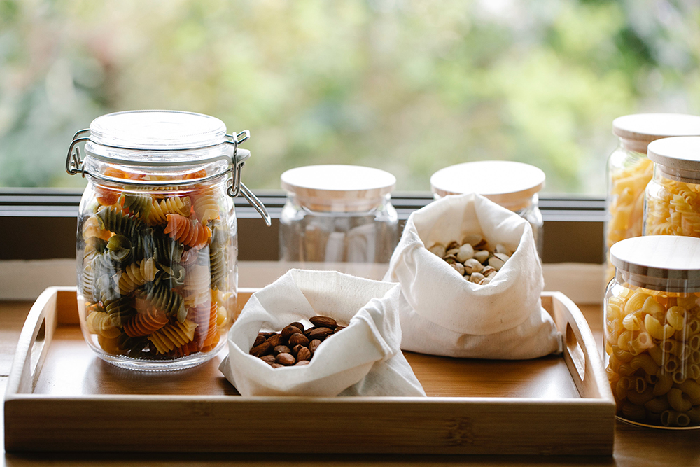 Jars of pasta, and linen bags of nuts on a kitchen counter top. 