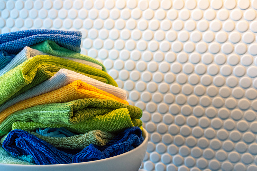 Stack of brightly colored dish rags in a bowl in front of a circle tiled back splash.