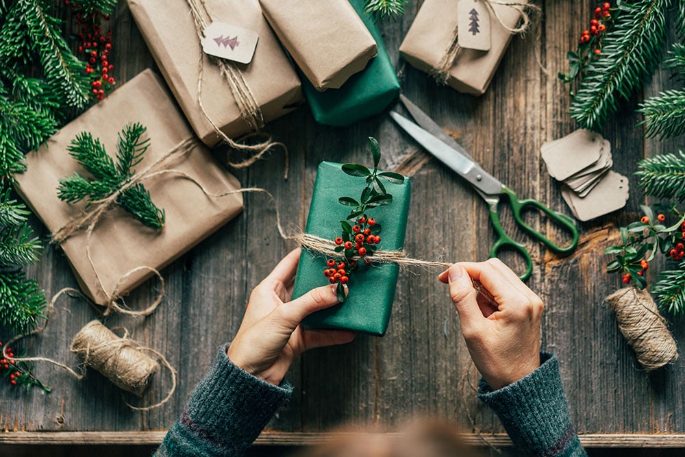 Flat lap of two hand wrapping holiday gifts with kraft wrapping paper and twine emphasizing sustainability.